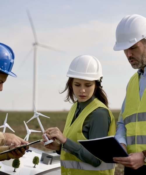 Team of caucasian and latin engineers standing on wind turbine field and discussing